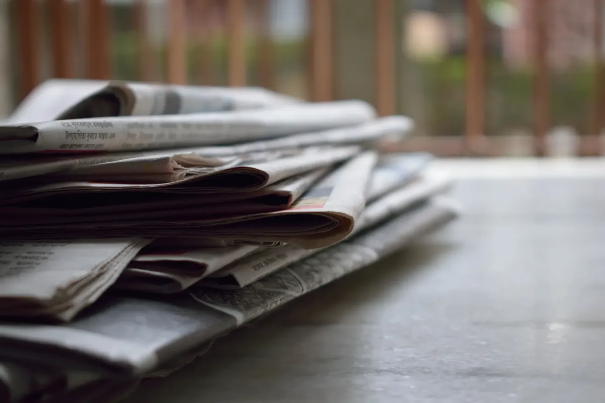 デスクの上に新聞が積まれた近景、情報とメディアを象徴しています
