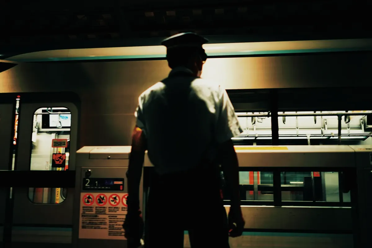 站內工人背影於夜間月台，監視電車到達。