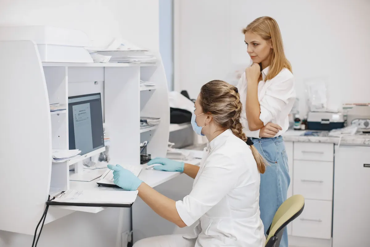 Two female healthcare workers in a clinical office, reviewing diagnostic results on a computer screen.