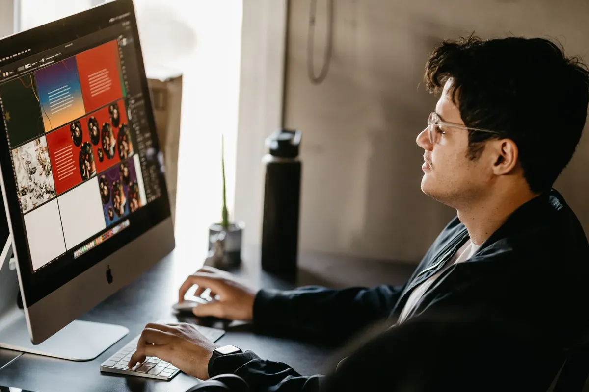 A focused graphic designer working on a computer in a modern office setting with creative visuals on the screen.