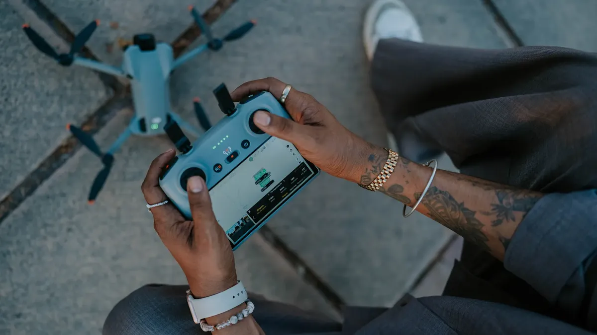 Tattooed hands operating a drone controller, emphasizing outdoor drone technology.
