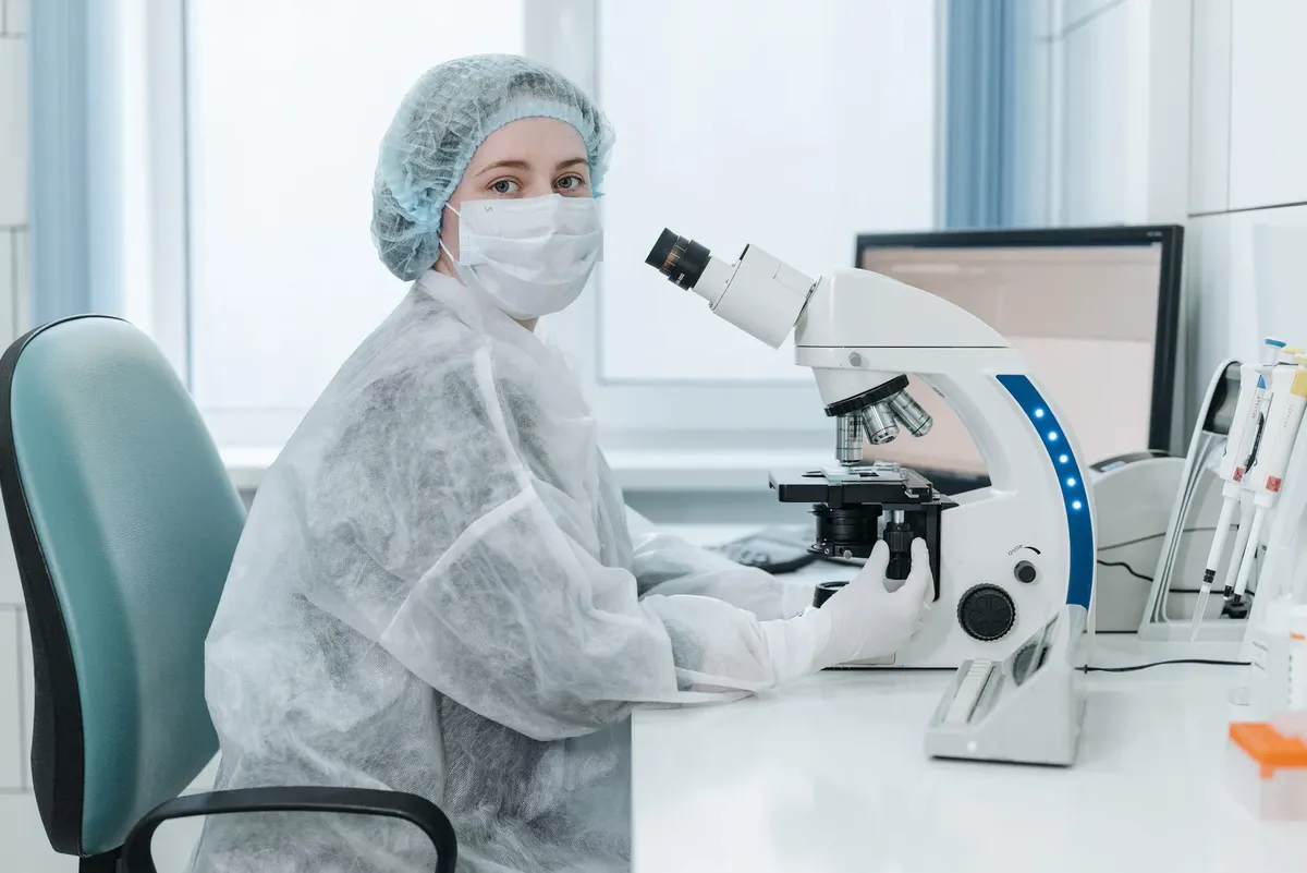 女性実験室技術者が三眼鏡を使ってサンプルを検査している医療実験室の様子です。