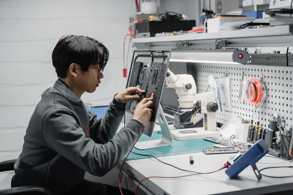 Focused young technician working on electronic repairs at a tech lab workspace.