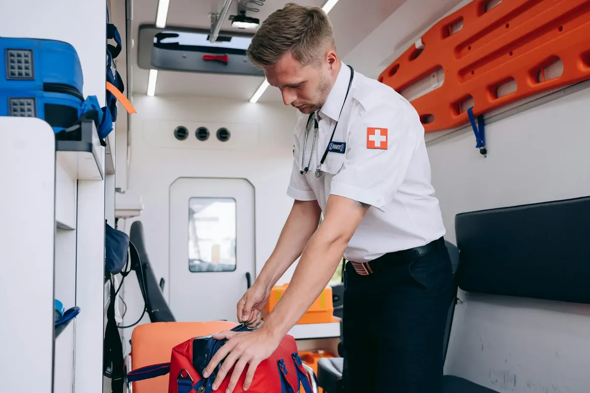 A paramedic in uniform organizes medical equipment inside an ambulance, preparing for emergency services.