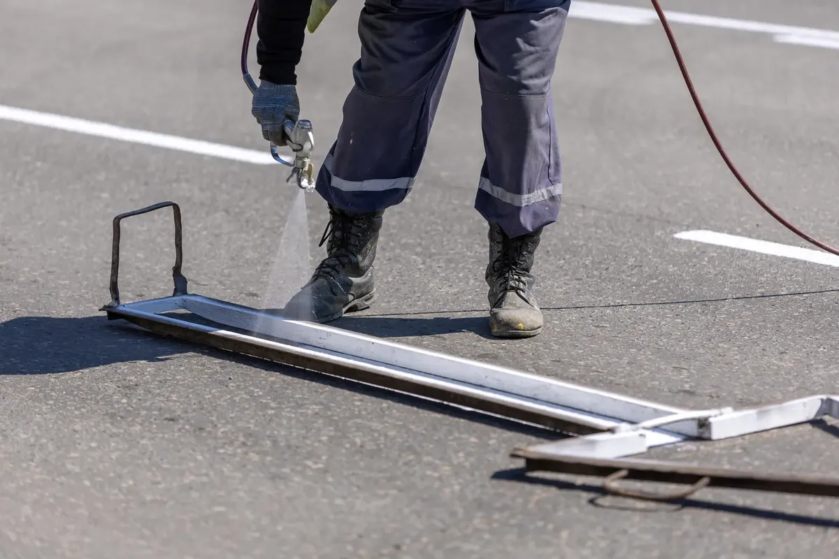 一名建築工人在白天使用噴槍在道路上繪製白線。