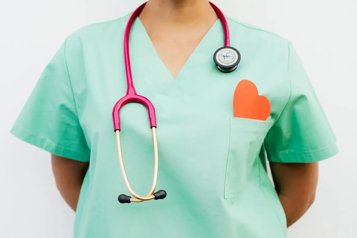 Close-up of a medical professional with a stethoscope and a paper heart cutout on a green uniform pocket.